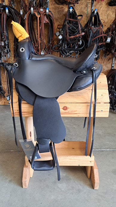 dp saddlery quantum short and light western with a western dressage seat, side view on a wooden saddle rack, horse tack in background